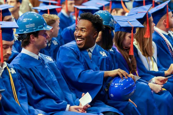 an engineering student sitting in the crowd at graduation. He's holding a UK hard hat.