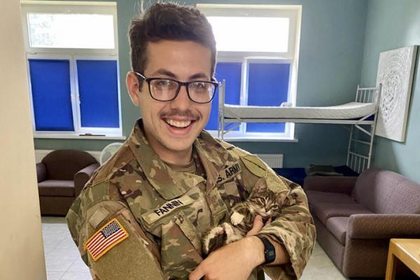Man in army uniform wearing glasses and holding a kitten while smiling