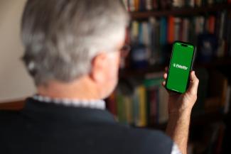 Man holding a phone with a Fidelity logo on it.