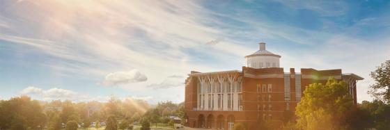 A sunny view of the William T. Young Library with wispy clouds and greenery in the foreground.