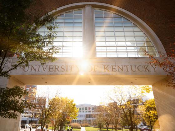 Sunset view of an arch that says "university of Kentucky" and a view of the medical campus in the background